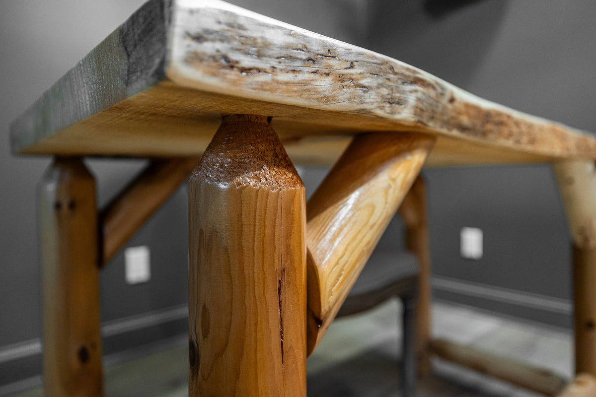 May include: A table featuring a natural live edge wood slab top with a light brown finish. The base is constructed from thick, cylindrical wooden logs with a smooth, polished finish, connected by angled support beams for structural stability.