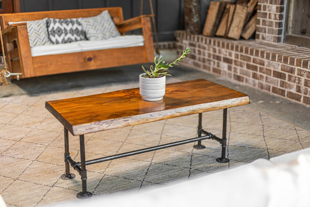 May include: A rustic wooden coffee table with a live edge top and black metal pipe legs. The table is sitting on a patterned rug in front of a white couch.