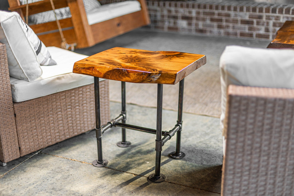 May include: A wooden table with a live edge top and black metal pipe legs. The table is sitting on a concrete patio.
