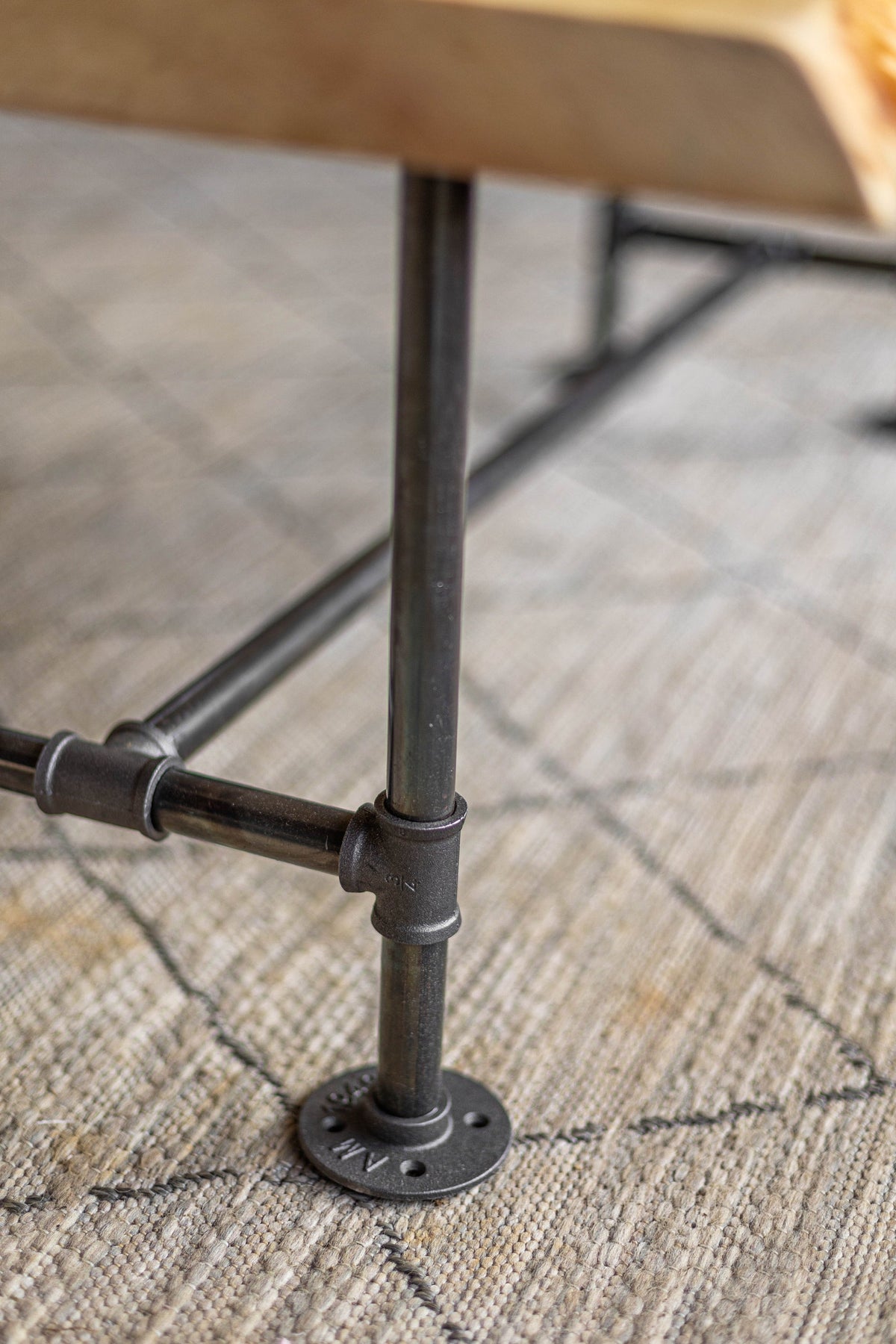 May include: Close-up of a black metal table leg with a pipe fitting and a round base. The table leg is on a patterned rug.