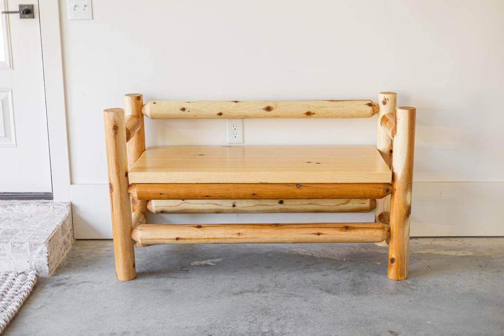 May include: A bench constructed from light-colored, unfinished logs featuring a smooth, flat seat and a backrest made of a single horizontal log. The structure is supported by four thick, vertical log legs with visible knots and natural wood grain.