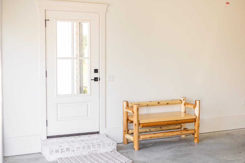 May include: A white door with a glass window pane and a black handle, positioned next to a rustic bench constructed from light-colored, unfinished logs. The bench features a smooth, flat seat and a backrest made of horizontal log segments.