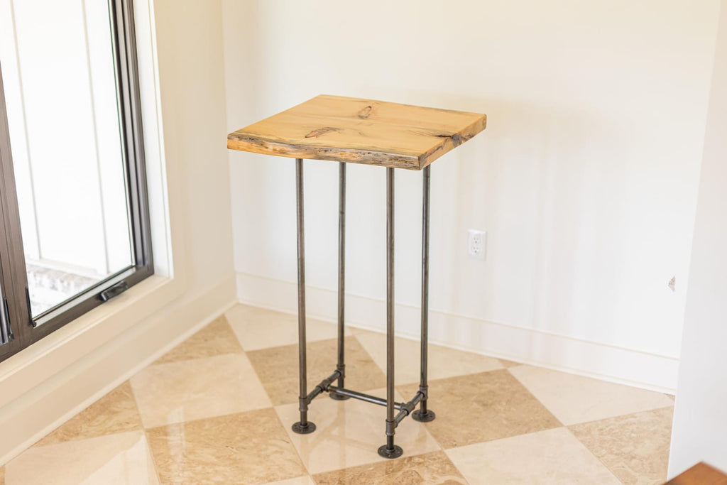 May include: A wooden table with a live edge top and a black metal pipe base. The table is standing on a tiled floor.