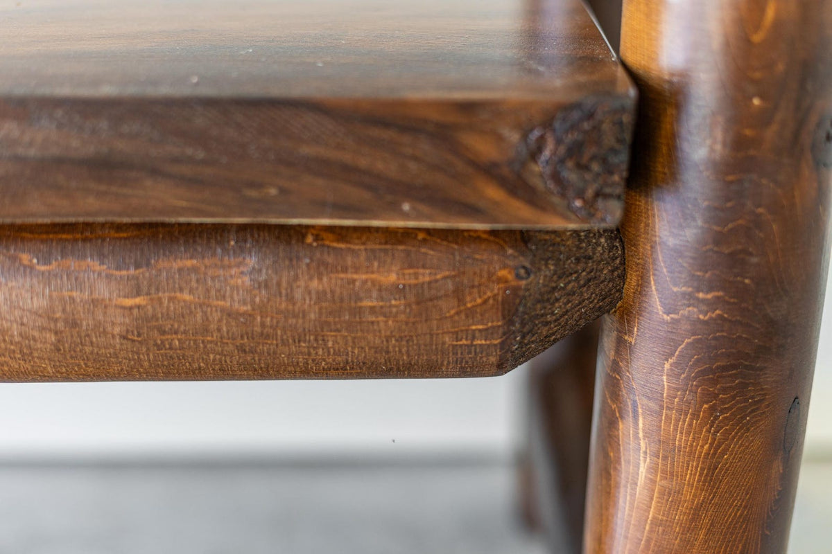 May include: A close-up view of a dark brown wooden furniture piece featuring a smooth, flat horizontal surface joined to a thick, cylindrical vertical support leg. The wood grain is visible throughout, showcasing natural textures and knots.