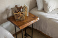 May include: A wooden end table with a live edge top and black metal legs. The table has a wire basket with wooden toys and a stack of books on top. The book on top has the word "Mississippi" printed on the spine.