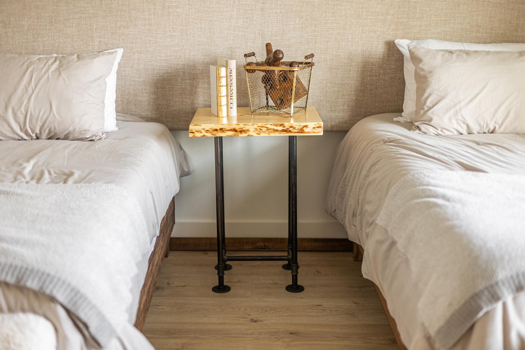 May include: A wooden bedside table with a live edge top and black metal pipe legs. The table is decorated with a wire basket filled with books and a decorative object.