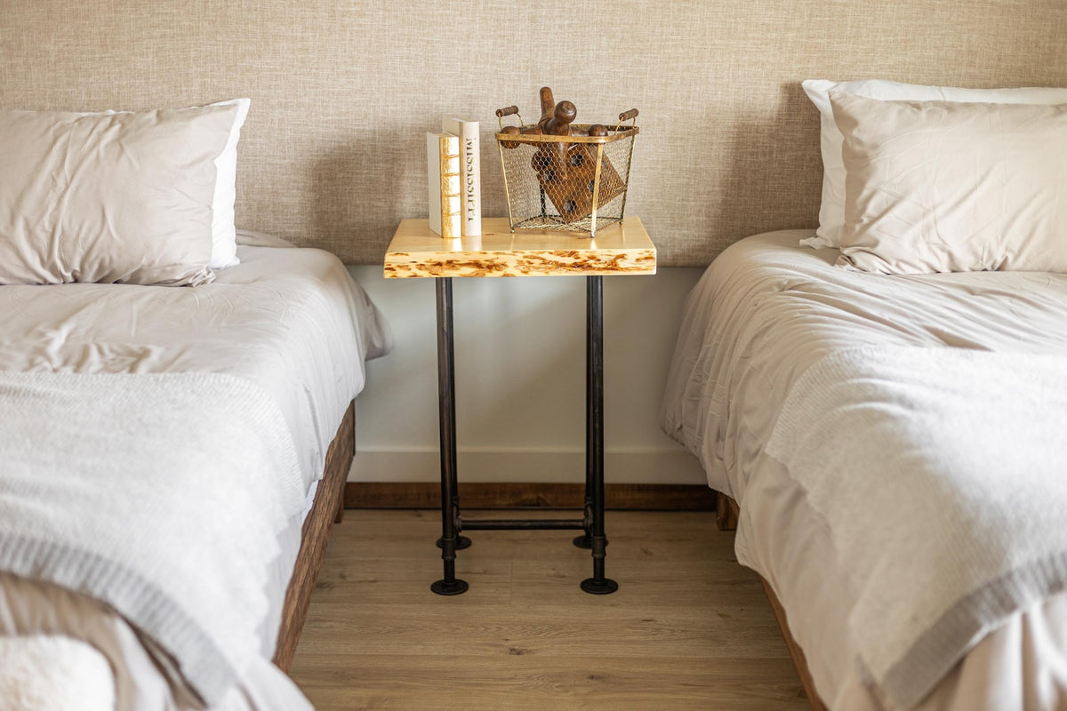 May include: A wooden bedside table with a live edge top and black metal pipe legs. The table is decorated with a wire basket filled with books and a decorative object.