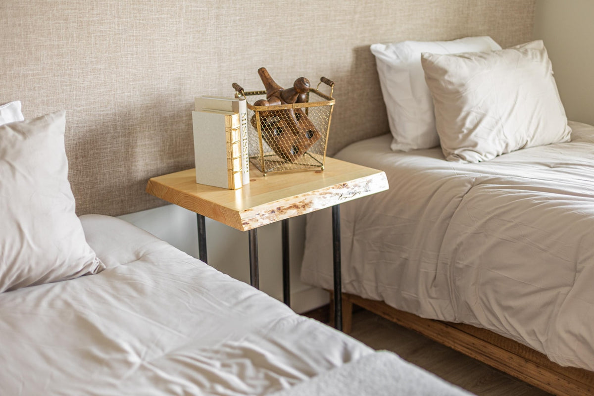 May include: Two twin beds with white linens and pillows, a wooden nightstand with a gold wire basket filled with wooden figurines and a stack of books.