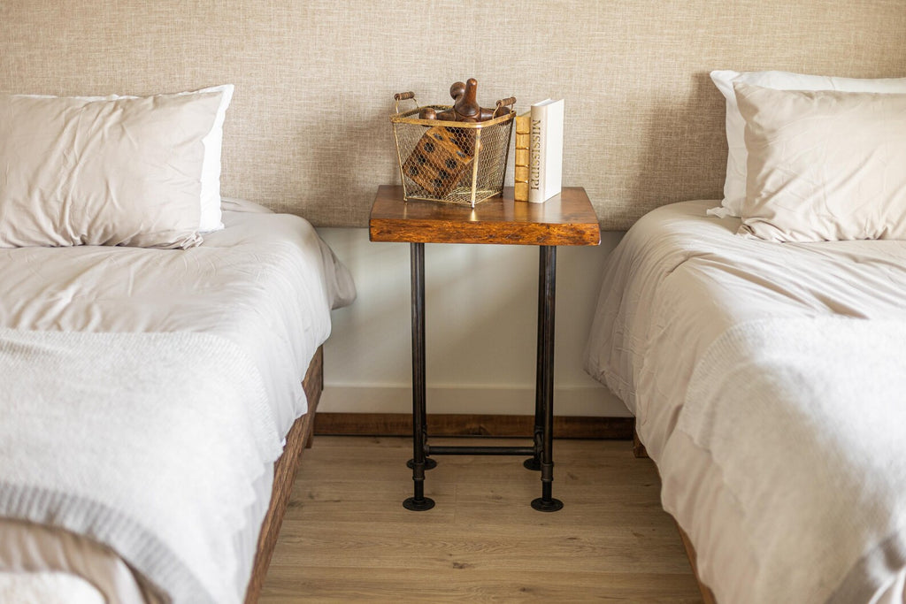 May include: A wooden bedside table with black metal legs. The table has a wooden top and a wire basket with decorative items on it. There are two books on the table.