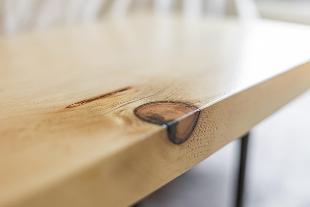 May include: Close-up of a light wood table top with a natural edge and a dark brown knot in the wood.