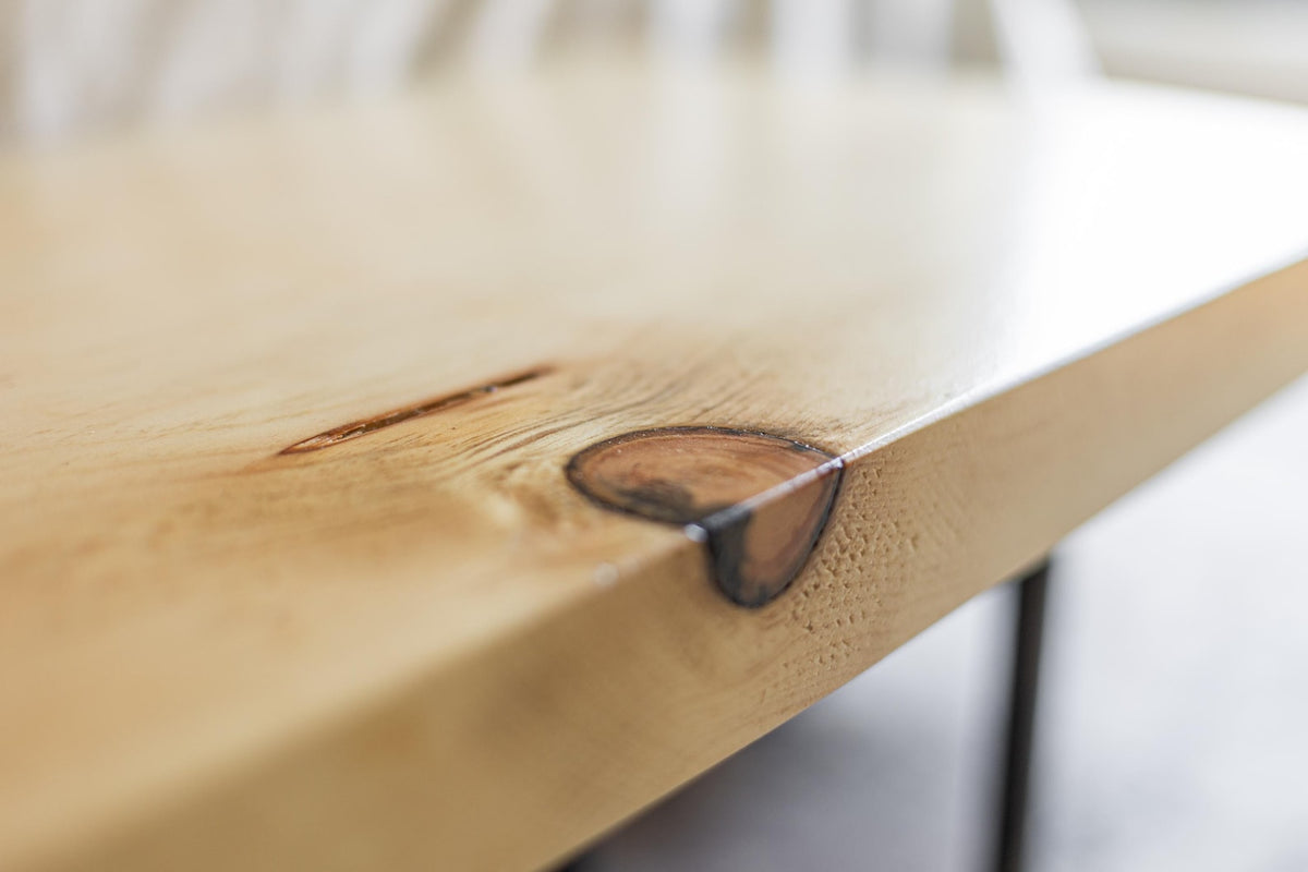 May include: Close-up of a light wood table top with a natural edge and a dark brown knot in the wood.