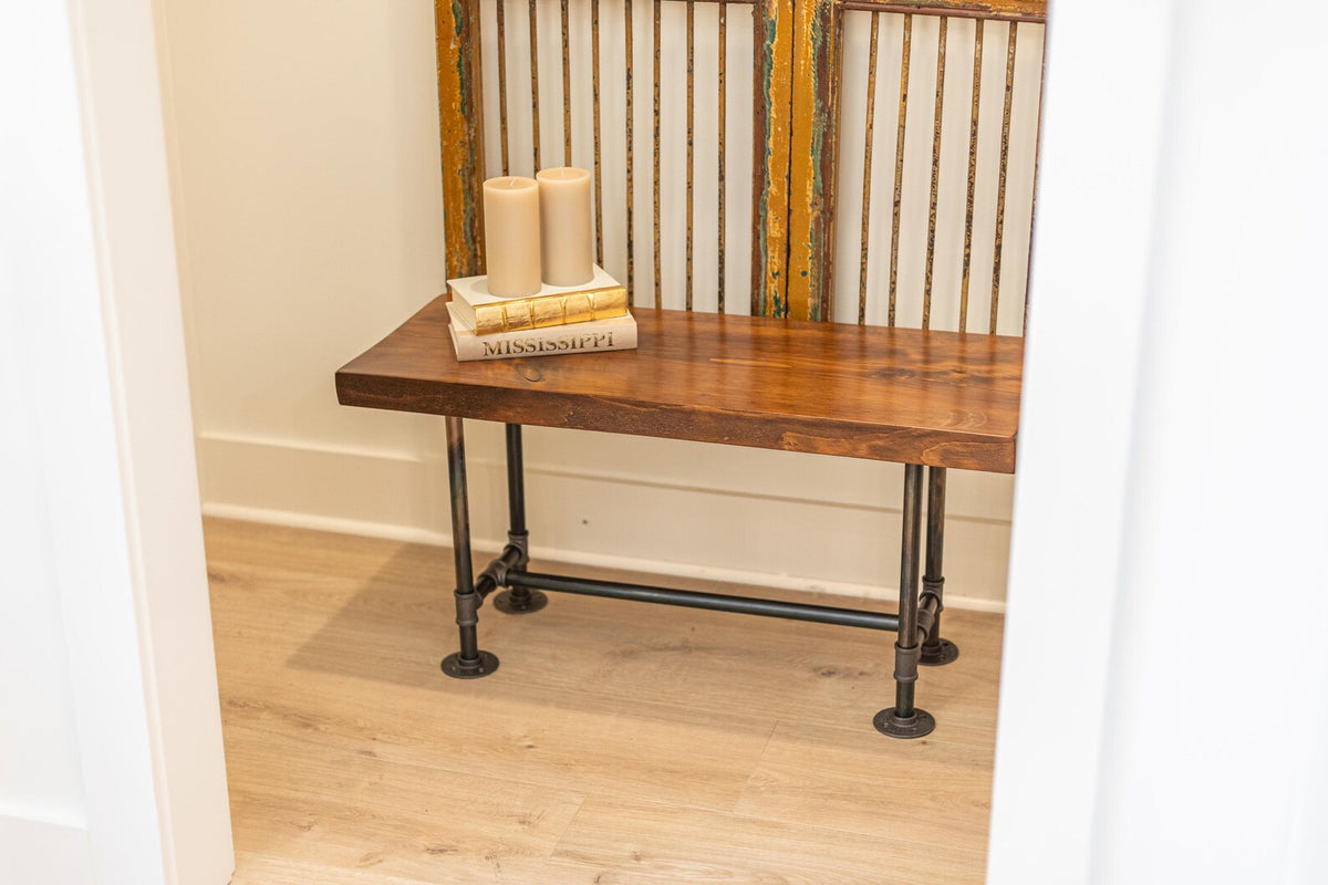 May include: A wooden bench with black metal pipe legs. The bench has a brown wooden top and is decorated with three candles and a stack of books. The books have the title "Mississippi" on the top book.