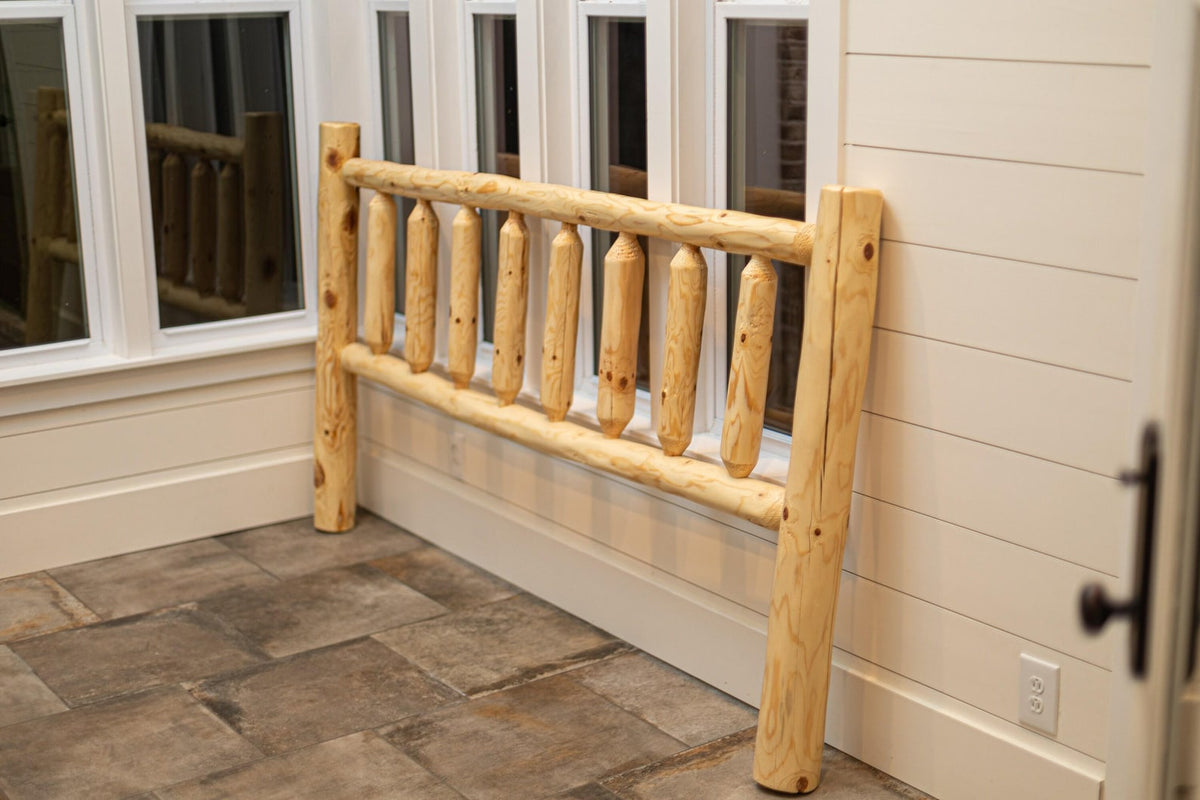 May include: A rustic, unfinished wooden headboard with a log cabin style. The headboard features vertical log posts and horizontal rails, creating a natural, outdoorsy aesthetic. The light-colored wood contrasts with the neutral-toned wall and floor.